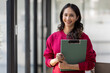 © David - Image of young indian girl asian woman, company worker document file in hand, smiling and holding digital tablet, standing over office background,business black woman holding a cup of coffee and files