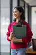 © David - Image of young indian girl asian woman, company worker document file in hand, smiling and holding digital tablet, standing over office background,business black woman holding a cup of coffee and files