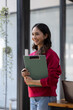 © David - Image of young indian girl asian woman, company worker document file in hand, smiling and holding digital tablet, standing over office background,business black woman holding a cup of coffee and files