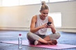 © Joanrae P/peopleimages.com - Exercise, relax and woman with phone on floor reading email or text after yoga workout at gym. Health, pilates and technology, girl on ground with smartphone checking fitness app online siting on mat