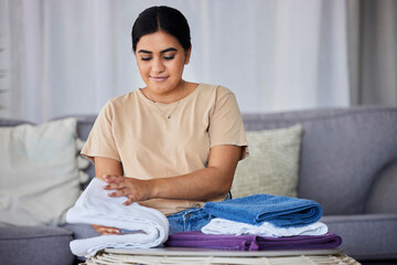 House, cleaning and woman fold laundry on a sofa, happy and relax alone in her home. Towels, housework and indian female relaxing while sorting fabric, linen and fresh cloth on the weekend or day off