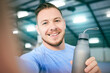 © C. D./peopleimages.com - Fitness, selfie and portrait of man with water bottle at gym for training, exercise and cardio on blurred background. Face, athletic and guy smile for photo while relax with drink during body workout