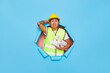 © South House Studio - Frustrated Asian industrial worker holds arm on a had has sorrowful expression dressed in uniform and safety helmet keeps paper blueprint poses through paper torn hole