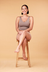 Wall Mural - Portrait, beauty and an asian woman on a chair in studio on a beige background for natural body positivity. Model, underwear and an attractive young female sitting on a stool with confidence