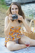 Happy smiling woman having picnic outside in nature wearing summer dress and photographs with vintage film camera
