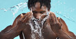 © Lou W/peopleimages.com - Water, splash and cleaning face for hygiene with a model black man in studio on a blue background for hydration. Bathroom, skincare or wellness with a male washing himself for natural skin treatment