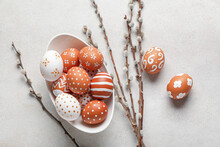 Bowl Of Painted Easter Eggs And Willow Branches On Light Background