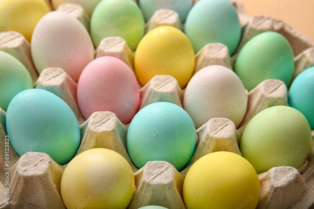 Cardboard holder with beautiful Easter eggs on color background, closeup