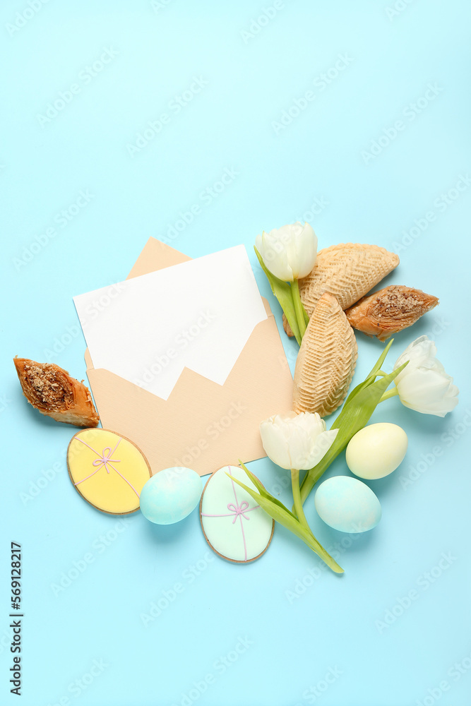 Envelope with blank card, flowers, eggs and treats on blue background. Novruz Bayram celebration