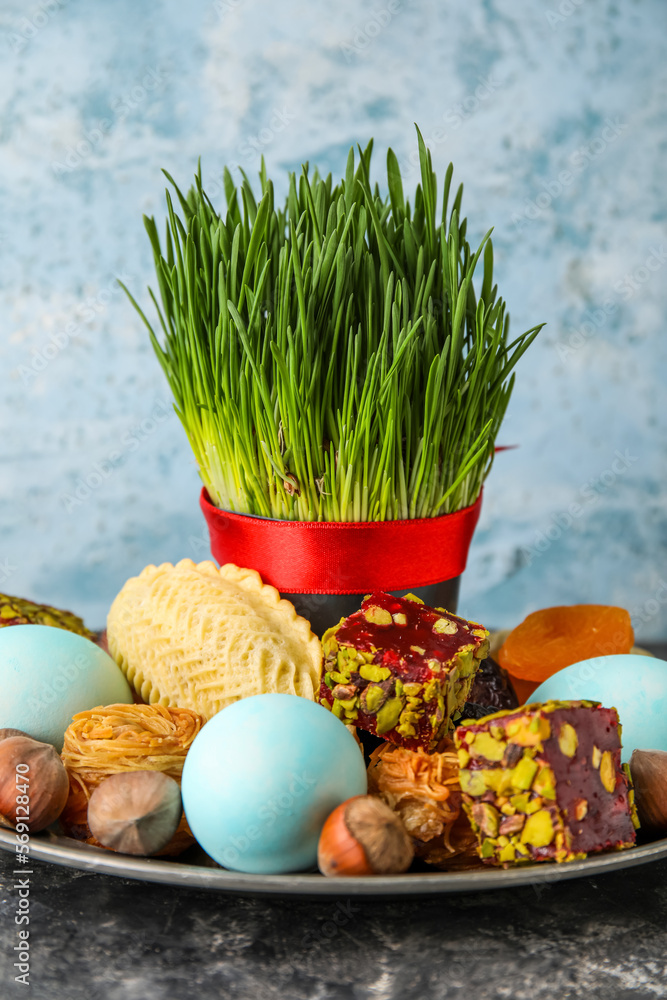 Plate with grass, eggs and treats on table near grunge wall. Novruz Bayram celebration