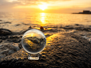 Wall Mural - glass ball on a rough stone by the ocean, sunset sky in the background. warm soft light. selective f