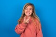 caucasian teenager girl wearing pink sweater over blue background holding an invisible aligner ready to use it. Dental healthcare and confidence concept.