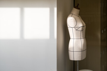 Empty tailor's textile female mannequin with black lines with sunlight on it for dressmaker working and designing new fashion collections with patterns and draping in an atelier tailor workshop.