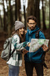 © Prostock-studio - Smiling young european people tourists in jackets with backpack walk in autumn forest, look at map