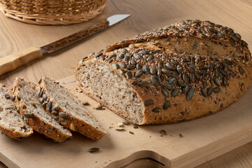 Wall Mural - Fresh loaf and slices of healthy spelt bread and a variety of seeds close up on a cutting board