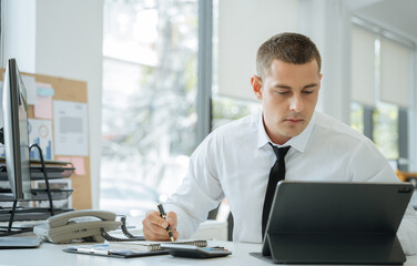 Businessman sitting at a table at home working on a laptop and writing down ideas in a notebook