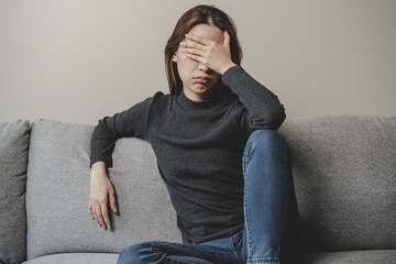 Wall Mural - Unhappy anxiety young Asian woman covering her face with pillow on the cough in the living room at home.