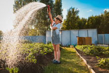 Child Watering Plants In Garden. Kid With Water Hose In Sunny Backyard. Little Girl Gardening. Summer Outdoor Activities During The Summer Holidays In The Village.