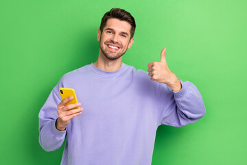 Poster - Photo of handsome guy toothy smile hold telephone show thumb up feedback isolated on green color background