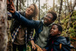 © Maskot - Father talking to woman and son while showing tree in forest during vacation