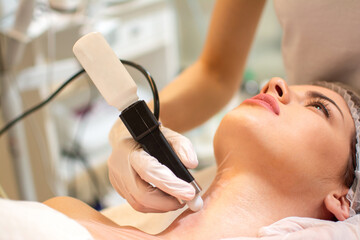 Wall Mural - Beauty doctor with ultrasonic scraber doing procedure of ultrasonic cleaning of female client's neck.