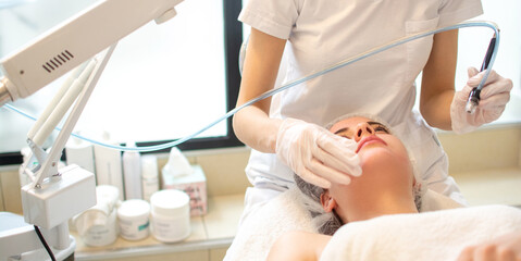 Wall Mural - Closeup headshot of young woman receiving hydrafacial therapy at beauty salon