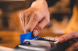 © chokniti - Closeup of hands of a young female cashier at barista swiping bank debit and credit card on NFC technology machine while processing payment for beverage and food ordered by customer