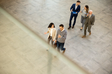 A group of young and senior business people are walking in an office hallway, captured in an aerial view. They are dressed in formal attire