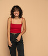 Young exotic happy brunette woman in red sleeveless shirt and jeans posing  on a beige background