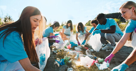 Wall Mural - Enthusiastic volunteers of different ages picking up plastic bottle, bags, cardboards, waste in gloves. Male and female activists putting garbage, trash, rubbish into bags. Eco-friendly concept.