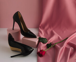 Contemporary fashion composition with elegant woman's high heels shoes on product podium, rose flower and pastel pink silk curtain. Valentine's Day or 8 March beauty concept.