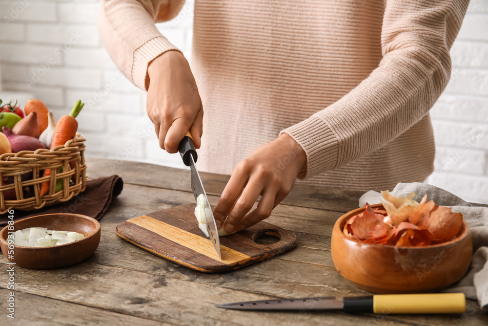 Woman cutting fresh onion on wooden table in kitchen