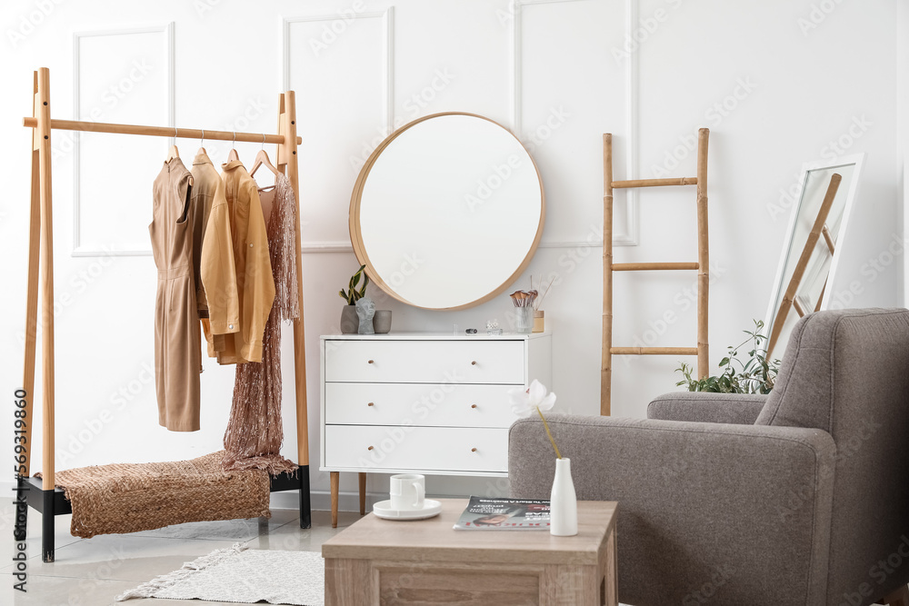 Interior of stylish dressing room with mirror, clothes and drawers