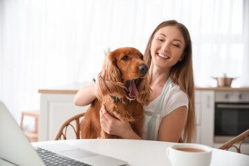 Wall Mural - Young woman with red cocker spaniel sitting at table in kitchen