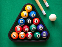 Spots and stripes balls in triangle, cue ball and two cues on the green table. Mini billiard, pool or snooker
