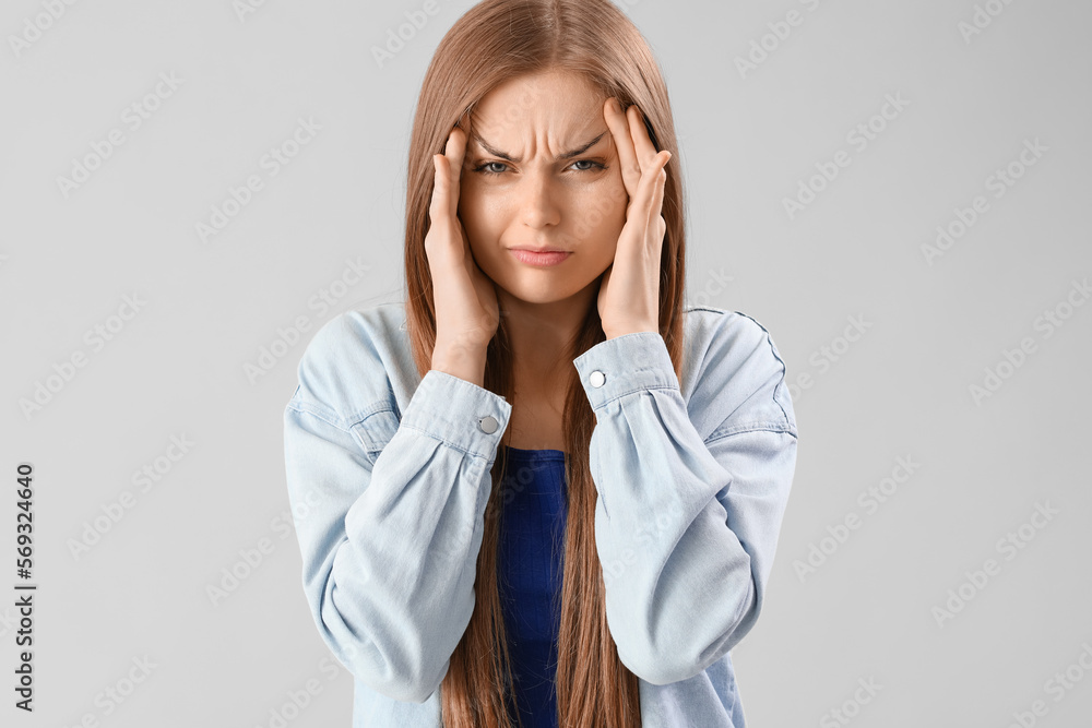 Young woman suffering from loud noise on grey background