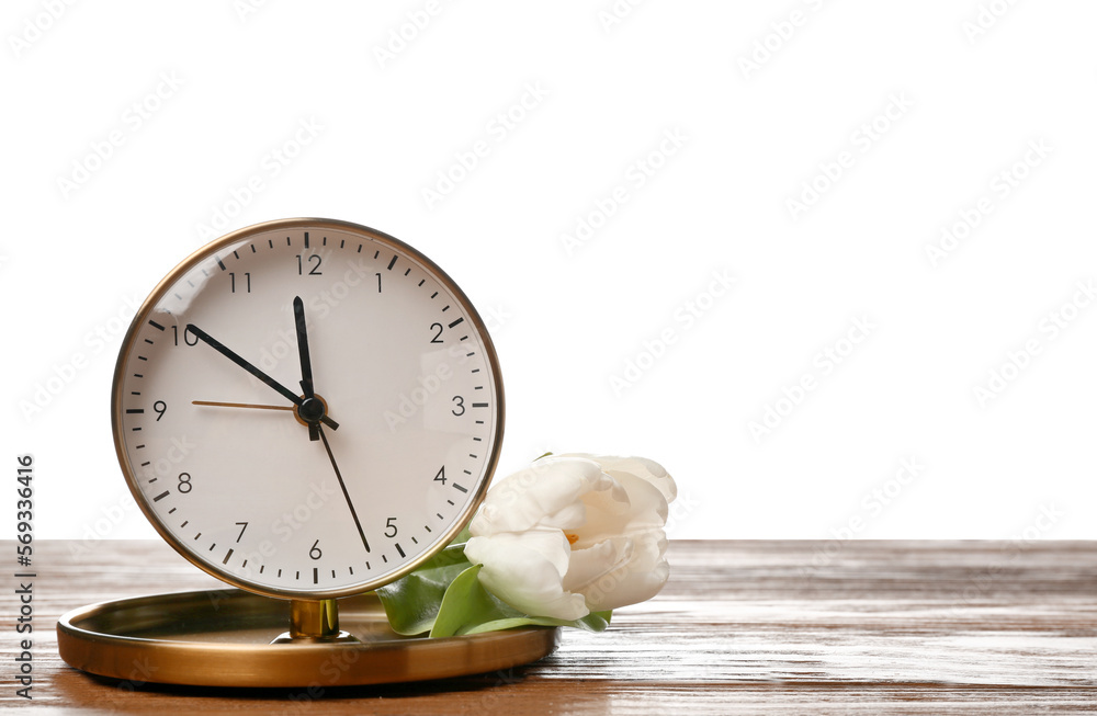Alarm clock and beautiful tulip on wooden table against white background