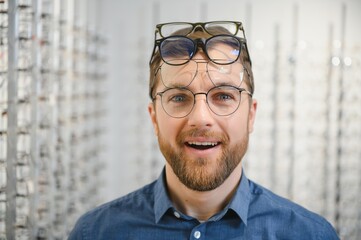 in optics shop. portrait of male client holding and wearing different spectacles, choosing and tryin