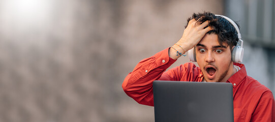 young man with headphones and laptop in the street with surprise expression