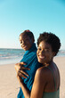 © wavebreak3 - Portrait of smiling african american mother covering daughter with towel at beach against clear sky