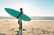 © WavebreakMediaMicro - Senior african american woman with surfboard standing on sandy beach against sea and sky at sunset