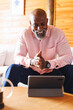 © Wavebreak Media - Bald african american senior man smiling and talking over video call on digital tablet in log cabin