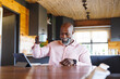 © Wavebreak Media - Bald african american senior man showing coffee mug over video call on digital tablet in log cabin
