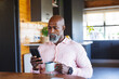 © Wavebreak Media - African american senior man with coffee mug and using smartphone while sitting at table in log cabin