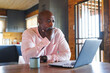 © Wavebreak Media - Serious bald african american senior man with hand on chin looking at laptop on table in log cabin