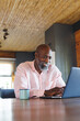 © Wavebreak Media - Smiling bald african american senior man with coffee mug on table using laptop in log cabin