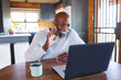 © Wavebreak Media - Happy african american senior man waving hand while talking over video call on laptop in log cabin