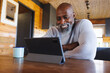© Wavebreak Media - Smiling bald african american senior man talking on video call over digital tablet in log cabin