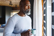 © Wavebreak Media - Thoughtful bald african american senior man with coffee mug looking through window at log cabin