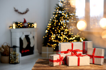 Many different gift boxes on wooden table against blurred festive lights in living room, space for text. Christmas presents